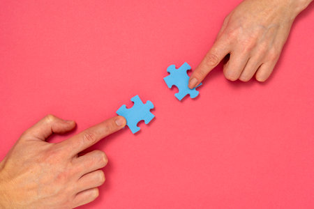 Hands of woman and man matching pieces of blue jigsaw puzzle on pink background. Relationship conceptの写真素材