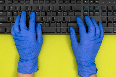 Closeup of black computer keyboard and hands in blue medical gloves. Work from home covid-19 concept.の写真素材