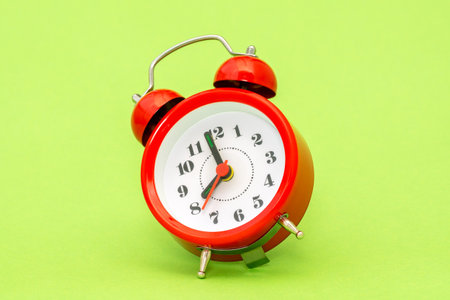 Vintage alarm clock falling on the green background. Red alarm clock showing 8 o'clock in a morning.の写真素材