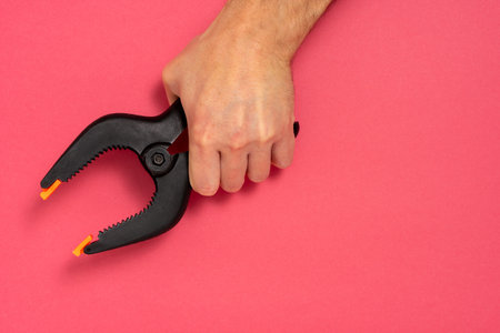 Hand holding large plastic spring clamp on pink background. Copy space.の写真素材