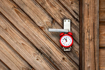 Red alarm clock hanging on the wooden door handleの写真素材