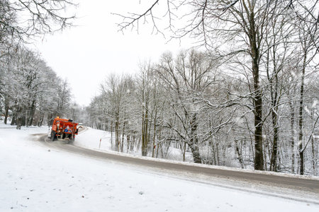 Snow ploughing truck cleans the road leading through the forest during a snowfallの写真素材