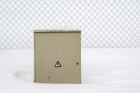 Outdoor Electric cabinet in the snowdrift next to fenceの写真素材