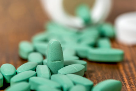 Green medical pills spilling out of a drug bottleの写真素材
