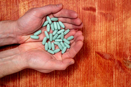 Medicine pills or capsules in hands over wooden background