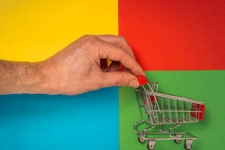 A hand pushing a red shopping cart on a colored backgroundの写真素材