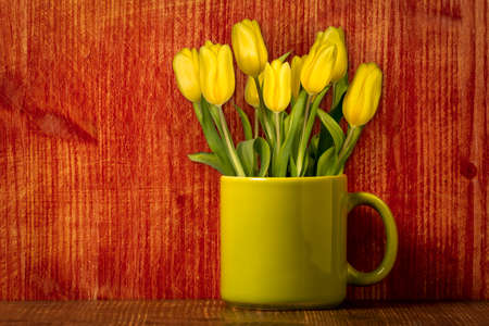 Coffee or tea mug with yellow tulips on the wooden backgroundの写真素材