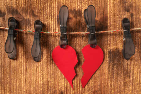 Broken paper heart hangs on clothespins on a wooden backgroundの写真素材