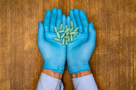 The doctor or pharmacist in blue gloves holding capsules in her handsの写真素材