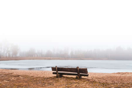 Empty bench at the frozen lake in the fogの写真素材
