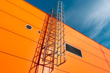 Orange industrial building wall with metal ladder,under blue skyの写真素材