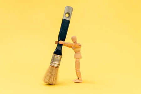 Wooden painter holding big paintbrush on the yellow backgroundの写真素材