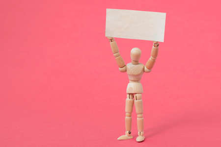 Wooden dummy holding blank placard on the pink backgroundの写真素材
