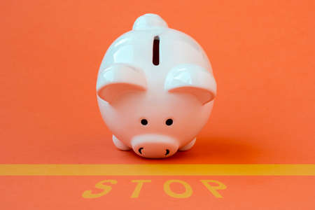 Piggy bank at the edge of a yellow line with a yellow print of the word STOP. Conceptual image.の写真素材