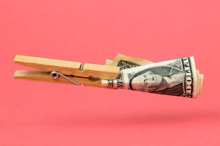 Wooden clothes pin with one dollar floating over pink backgroundの写真素材