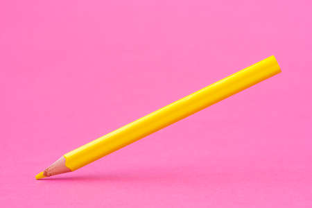Yellow color pencil levitating over a pink background. Copy space.