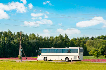 The white bus traveling on the road  in a rural landscape under a blue sky with white cloudsの写真素材