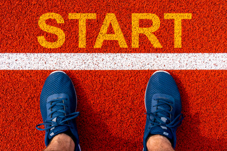 Man legs in sport sneakers standing next to line and word START on running trackの写真素材