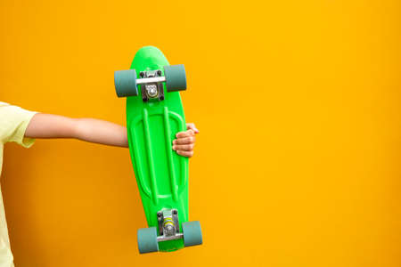 Youth culture. Hand with green penny board against  yellow urban wall with empty space for text