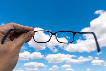 Out of focus cloudy sky with hand holding a glasses that correct the visionの写真素材