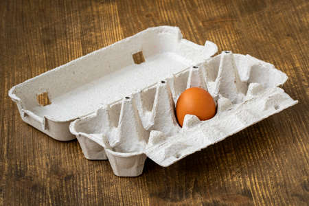 One brown egg in a cardboard egg carton on wooden backgroundの写真素材