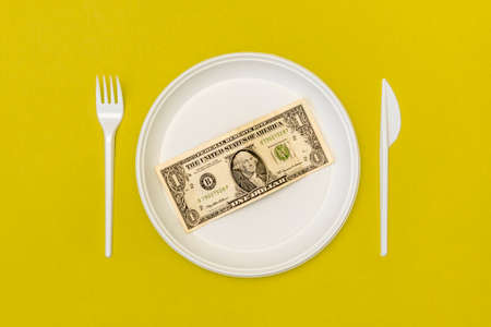 Top view of disposable cutlery and plate with dollar bill on yellow background. Money concept.の写真素材