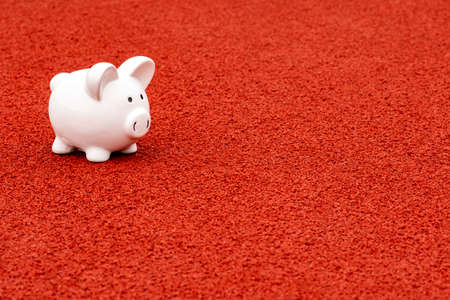 White piggy bank standing on the red rubber surface in the sports stadiumの写真素材