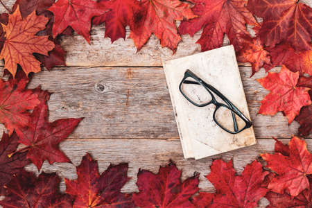 Old book, eye glasses and autumn leaves on wooden tableの写真素材