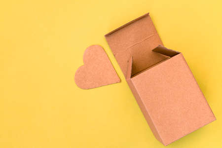 Open cardboard box and heart cutted from cardboard lying on the yellow backgroundの写真素材