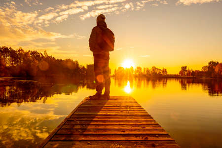 Back view of adult man standing on pier facing to the sunsetの写真素材