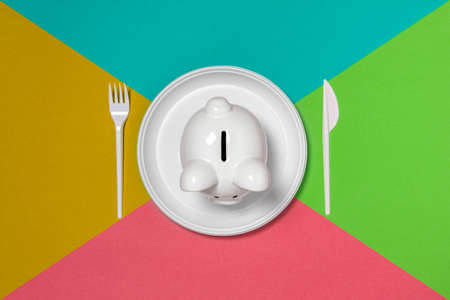 Eat up savings or savings consumer concept. Piggy bank on the plate with fork and knif.の写真素材