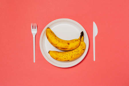 A white plate with ripe bananas and fork with knife on the pink background. Healthy eating.の写真素材