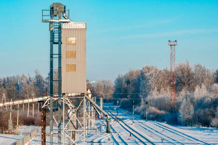 Metal grain elevator next to railroad during winter season. Grain silo, warehouse or depository is...