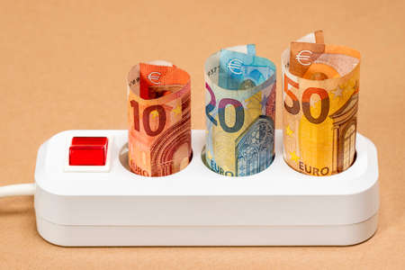 Euro money banknotes inserted into an extension socket. Increasing cost of electricity for business users and residential customers. Rise in electricity prices concept.の写真素材