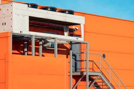Air conditioner units on a orange wall of industrial buildingの写真素材