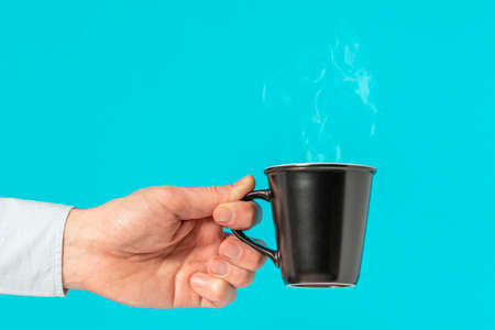 Hand of a man holding a hot coffee cup with smoke on the blue background