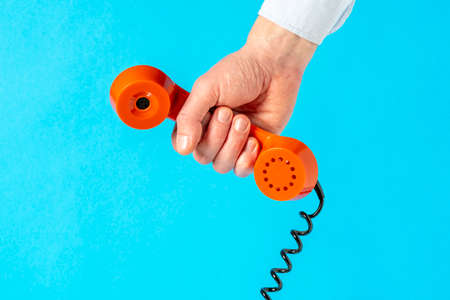Hand holding old telephone receiver over blue background.Communication concept.の写真素材