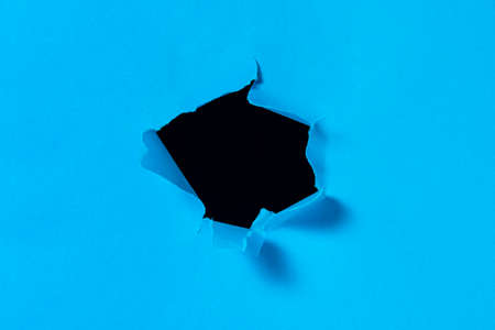 A hole in blue paper with torn edges and a black isolated background inside. Ripped blue paper, copy...