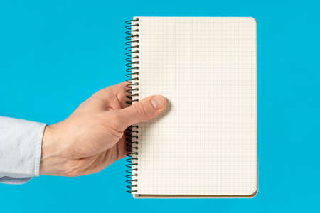 Man hand holding a notebook with square grid. Blank sheets for text.