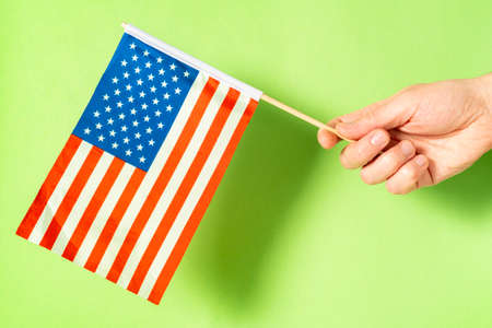 Hand holding small american flag on green background