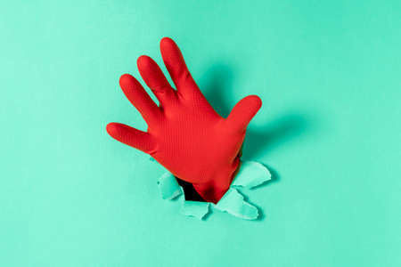 Hand in red rubber glove sticks out of a torn hole in blue paper
