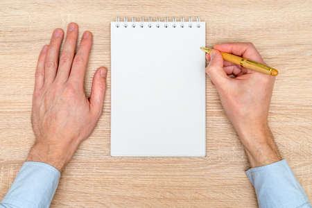 Hand writing in white blank open spiral notebook with pen on wooden background. Flat lay, copy space. Creative work, business, finance or education conceptの写真素材