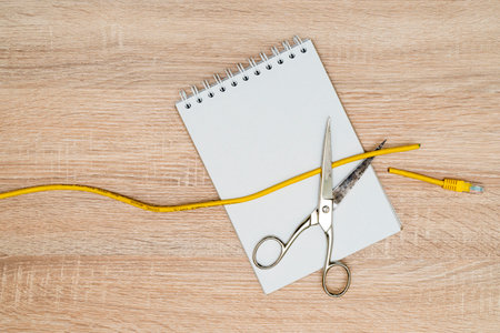 Scissors cutting data cable over a blank spiral notebook. Concept of global internet outageの写真素材
