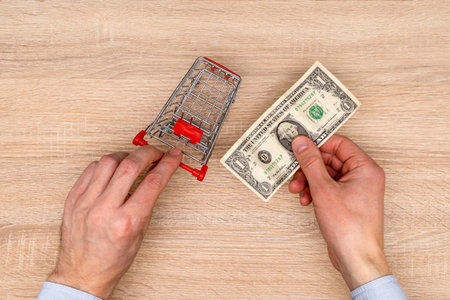 Businessman pushes the toy cart and holds one dollar bill in the hand. Shopping concept