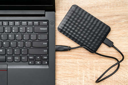 A portable hdd connected to a laptop on a wooden background, top view. The concept of data storageの写真素材