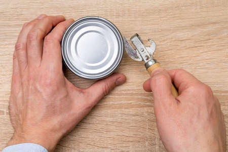 Man opening a can with a can opener. Canned food.の写真素材