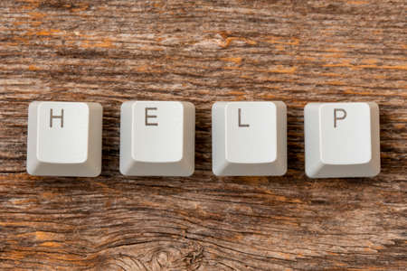 Four computer keyboard keys arranged to spell HELP word on the wooden background