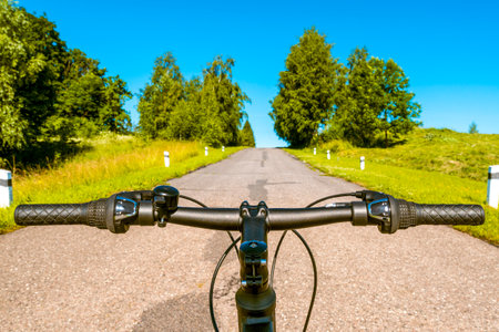 First person view of handling the bicycle on the empty asphalt road.Concept of world bicycle day, healthy lifestyle, cycling and sports activity in nature.の写真素材