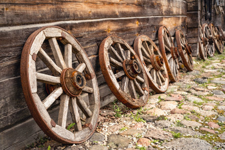 Row of old wooden wagon wheels leaning on a log cabin.の写真素材