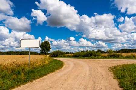 A country road splits in two, making a decision-requiring fork in the road. Concept image. Empty road signpost for your text.の写真素材